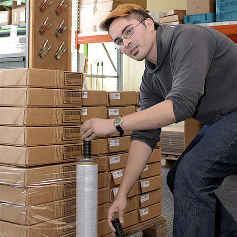 Mann mit Folienrolle verpackt Kartons zu Versandgebinde